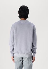 Grå oversized sweatshirt med en blød tekstur, rund hals, ribbede manchetter og talje, præsenteret fra ryggen mod en ensfarvet baggrund.