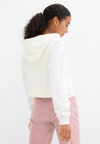 Felpa bianca corta con cappuccio, orlo e polsini a coste, abbinata a pantaloni in velluto a coste rosa chiaro con tasche posteriori e tessuto strutturato.