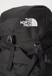 Svart North Face ryggsekk med toppflap, justerbare stropper og to plastspenner foran som sikrer hovedrommet.