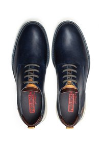 Chaussures en cuir bleu marine avec une texture perforée, bout rond et lacets gris. Présente un détail de talon marron contrasté et une semelle intérieure texturée.