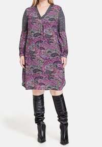 Långärmad klänning med ett lila, grönt och svart paisleymönster, med en djup V-ringning och kontrasterande grå mönstrade ärmar.