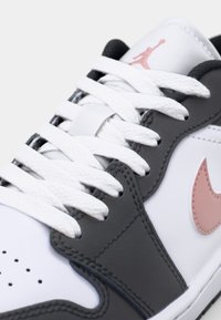 Białe i szare sneakersy z białymi sznurówkami, różowym logo Nike na boku oraz różowym logo Jumpman na języku.