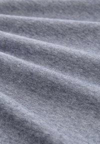Denim látka v tlmených šedých farbách s jemnými vertikálnymi pruhmi. Mäkka textúra s mierne lesklým povrchom, so znateľnými záhybmi a skladmi.