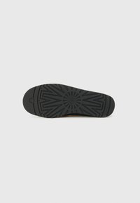 Suola di scarpa in gomma nera con un motivo di grip testurizzato, emblema circolare e design con bordo arrotondato.