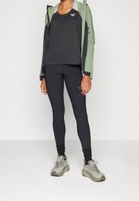 Schwarzes sportliches Tanktop und Leggings unter einer hellgrünen Jacke, kombiniert mit grauen Turnschuhen, mit einem schlanken Design und einer enganliegenden Textur.