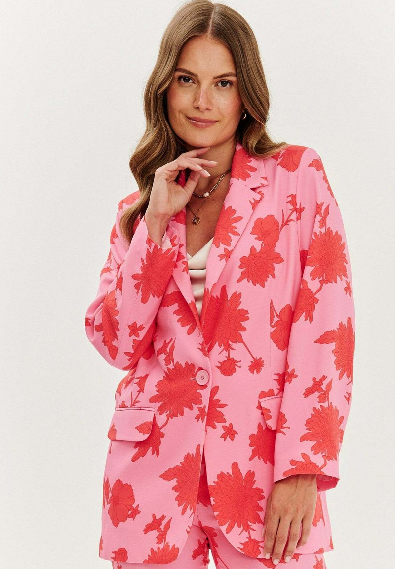 Růžový květinový blejzr s červenými květinovými vzory, s jedním knoflíkem, dvěma předními kapsami a uvolněným střihem. Hladká textilie.