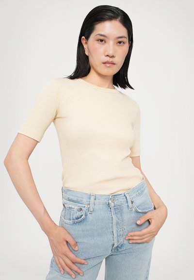 Cream ribbed short-sleeve t-shirt with a round neckline, paired with light blue high-waisted denim jeans. Smooth texture, fitted design.