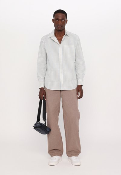 Striped button-up shirt in light colors, beige wide-leg pants, and white sneakers. Holding a dark bag with a shoulder strap.