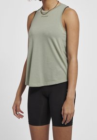 Ljust grön ärmlös tanktopp med ett strukturerat mönster och en rundad halsringning, tillsammans med svarta åtsittande shorts.