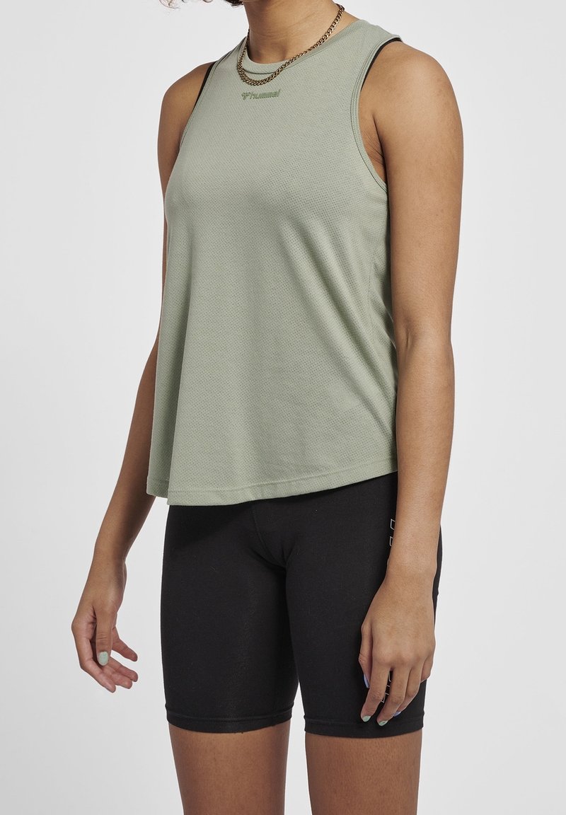 Ljust grön ärmlös tanktopp med ett strukturerat mönster och en rundad halsringning, tillsammans med svarta åtsittande shorts.