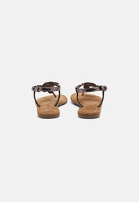 Brown suede sandals featuring a thin strap design with a scalloped edge and a buckle closure, flat sole with light tread pattern.