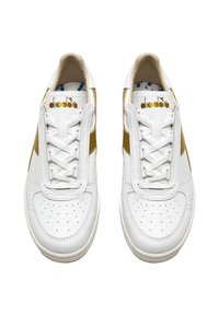 Sneaker in pelle bianca con una striscia laterale dorata, punta traforata e lacci bianchi. Logo Diadora in oro sulla linguetta.