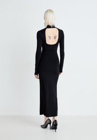 Μαύρο φόρεμα με μακριά μανίκια και εφαρμοστή σιλουέτα, με ανοιχτή πλάτη. Διαθέτει τατουάζ πεταλούδες και ψηλές γόβες από δίχτυ.