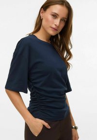 Marineblå t-shirt med korte ærmer og rund hals samt detaljer med rynkning i siden, lavet af blød bomuldsstof, som giver en afslappet pasform.