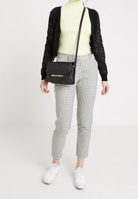 Svart öppenstickad cardigan, ljusgrön mötkrage, rutiga byxor och vita sneakers. Axellväska med guldfärgad detalj.