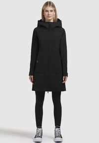 Black long jacket with a hood, full front zipper, and side pockets. Features a sleek design and a smooth texture. Worn over leggings and sneakers.