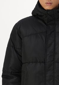 Black puffer jacket with a high collar, featuring a smooth texture, visible stitching, and a button closure. Suitable for cold weather.