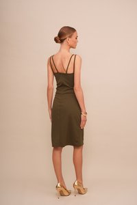 Robe ajustée vert olive avec des fines bretelles et une fermeture éclair au dos, longueur genou, assortie à des talons hauts dorés. Texture de tissu lisse, design minimaliste.