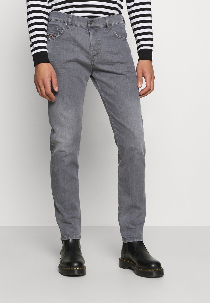 Harmaat farkut, joissa on istuva malli, viiden taskun tyyli ja hienovaraiset ompeleet, yhdistettynä mustiin nilkkureihin.