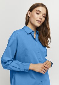 Camicia azzurra chiara con colletto, maniche lunghe e due bottoni ai polsini. Tessuto morbido con una vestibilità comoda e senza pattern visibili.