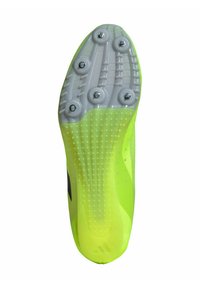 Zapato deportivo con cleats de un vibrante color amarillo de material sintético. Presenta una suela de goma blanca con seis clavos metálicos y patrones de agarre texturizados.