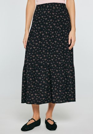 Czarna spódnica midi z małym różowym kwiatowym nadrukiem, warstwowy design, noszona z czarnymi balerinami Mary Jane i jasnoróżowym topem.