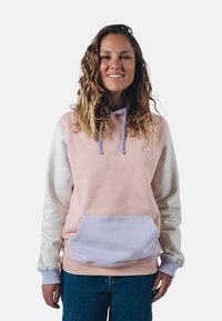 Mikina s kapucí v pastelově růžové a bílé barvě, s přední kapsou, měkkou texturou a kontrastními levandulovými šňůrkami. Vybavena vyšívaným logem.