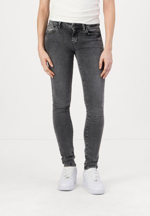Jean gris ajusté avec un délavage, doté de cinq poches et d'une fermeture à boutons. Porté avec des baskets blanches sur un fond uni.