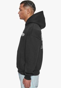 Black hooded sweatshirt with a front pocket, featuring white graphic text on the chest and back, made from soft, textured fabric.