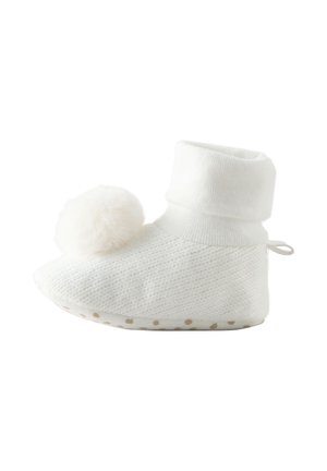 Chausson de bébé tricoté blanc doux avec cheville rabattue, grand pompon sur le dessus et semelle antidérapante à pois.