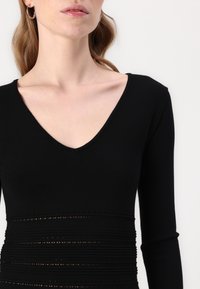 Black long-sleeve top with a V-neck, featuring horizontal textured stripes and a form-fitting design. Made from a smooth fabric.