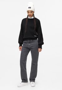 Mustmust, mille õlgadega ja hallide sirgete pükstega. Mudel kannab valget beanie'd, millel on logo ja valgeid sneakers'e.