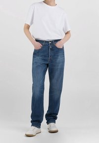 Lättvikts vit bomullströja i kombination med högmidjade blå denimjeans. Jeansen har en klassisk femfickdesign och lätt blekning.