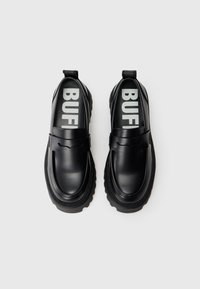 Melnās slip-on kurpes, kas izgatavotas no gludas ādas ar rievotu gumijas zoli. Iekšējo zoli rotā dekoratīvs siksniņa un "BUFF" logo.