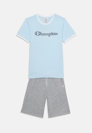 Svijetloplava pamučna majica kratkih rukava s bijelim obrubom i "Champion" logom, uparena s sivim pamučnim kratkim hlačama s elastičnom pojasom i logotipom.