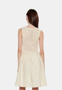 Vestido sin mangas color crema con un corpiño de crochet y una falda acampanada y texturizada. La parte posterior muestra un patrón de punto abierto.