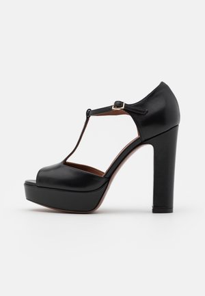 Schwarzer Leder Plateau High Heel Schuh mit T-Riemen und Schnallenverschluss, Peeptoe und klobigem Blockabsatz auf weißem Hintergrund.