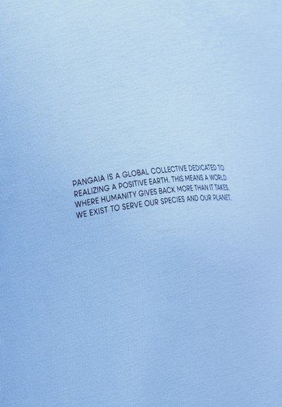 Το κείμενο σε ανοιχτό γαλάζιο ύφασμα λέει: «Η Pangaia είναι ένα παγκόσμιο συλλογικό που έχει αφιερωθεί στη δημιουργία ενός θετικού πλανήτη, όπου η ανθρωπότητα επιστρέφει περισσότερα από όσα παίρνει.»