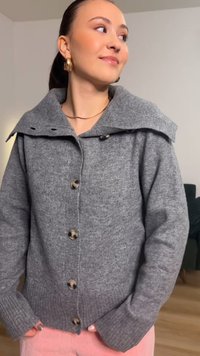 Harmaa neulottu neuletakki, jossa on leveä kaulus, isot napit ja resorireunukset hihoissa. Kangas on pehmeän tekstuurinen.