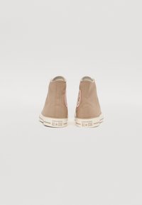 Baskets montantes en toile marron avec écusson logo rose à l'arrière, semelle en caoutchouc blanche et détails de coutures contrastantes.