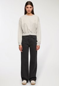 Sweatshirt grigio, corto, con maniche lunghe e fondo a coste, abbinato a jeans neri a vita alta e gamba larga, e sneakers bianche.