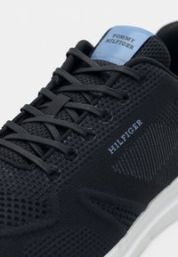 Tamsiai mėlyni Tommy Hilfiger sportbačiai su tinklinio dizainu, juodomis raištelėmis ir balta padais, rodomas prekės ženklas šone ir ant liežuvėlio.