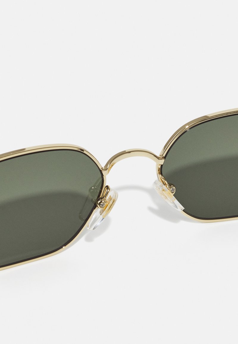 Gold-framed sunglasses with dark green lenses. Features include clear nose pads and a curved bridge connecting the lenses.