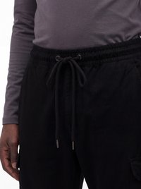 Person trägt schwarze Kordelzug-Hose und ein graues Langarmshirt, zeigt eine Nahaufnahme der Taille und Hand.