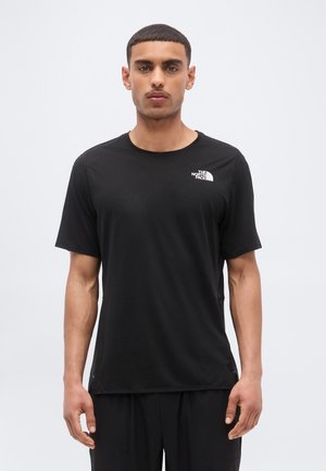 Mann iført en ensfarget svart The North Face t-skjorte, stående foran en lys grå bakgrunn, ser rett frem med nøytralt uttrykk.