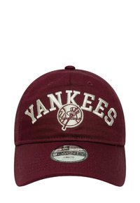 Maroon baseball cap with "YANKEES" embroidered in white. Features a rounded visor and adjustable strap. Includes a logo patch on front.