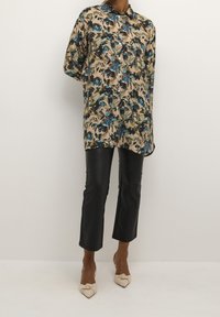 Chemise à motif floral, tons beige et bleu, manches longues, à boutons. Pantalons cropped en simili cuir noir. Talons knottés beige.