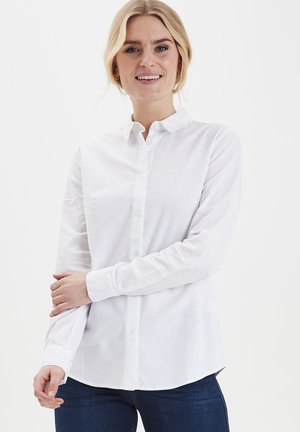 Camicetta bianca con bottoni realizzata in tessuto leggero, caratterizzata da maniche lunghe, colletto e orlo curvo, abbinata a jeans in denim blu.