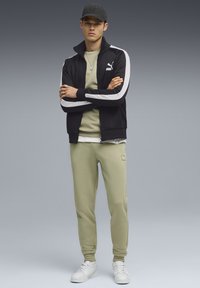 Sort zip-jakke med hvide striber, lys grøn T-shirt, matchende bukser og hvide sneakers. Har Puma-branding. Glat tekstur.
