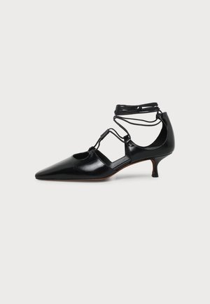 Chaussure en cuir noir à bout pointu et talon kitten, avec lacets à nouer autour de la cheville et découpes latérales sur fond uni.